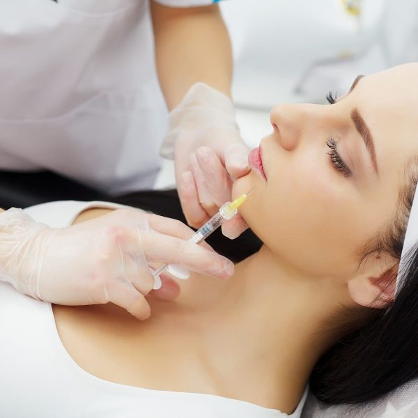 Woman receiving a botox injection in the lips zone lying in bathrobe on the medical couch